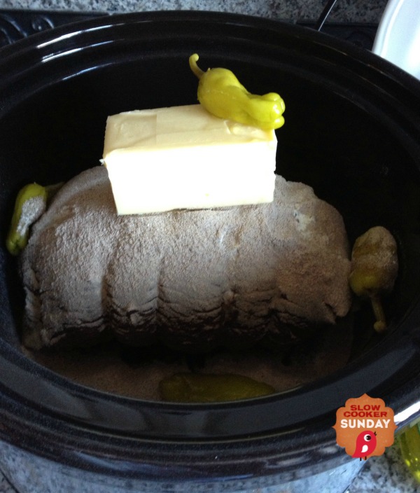 beef roast in a crockpot with a stick of butter on top. 