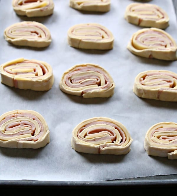 turkey and cheese pinwheels lined up on baking sheet ready to be baked. 