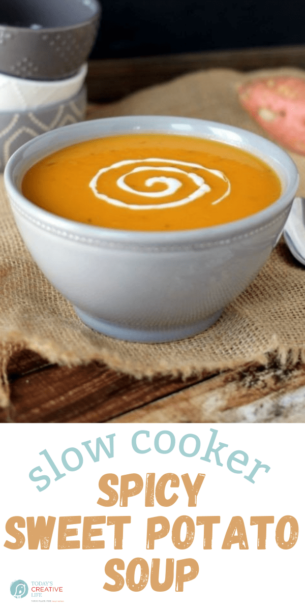 A bowl of slow cooker spicy sweet potato soup with sour cream swirled on top.