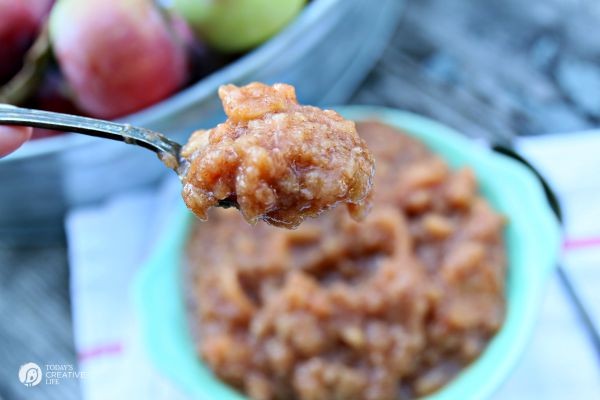 Homemade Slow Cooker Applesauce dripping off a spoon with a bowl of applesauce in the background.
