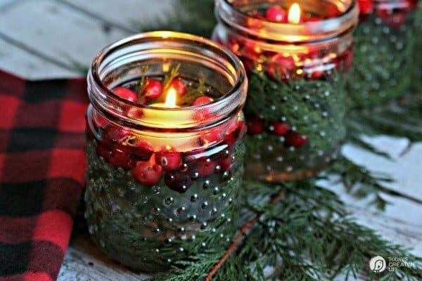 Jars filled with water, cedar and cranberries with a floating candle lit.