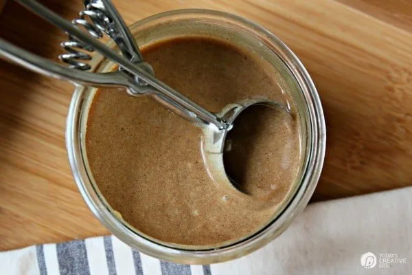 looking down into a jar of hot buttered rum mix with a small ice cream scooper inside. 