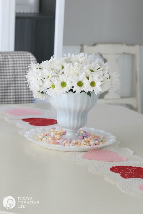 10 Minute Valentines Table Decor | create a quick, simple and easy Valentine's Day decorations tablescape centerpiece with a heart shape doily table runner, conversation hearts and daisies. See more on Today's Creative Life. 