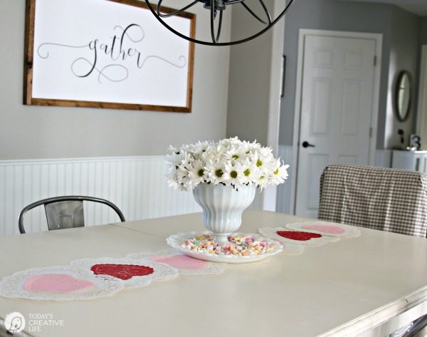 10 Minute Valentines Table Decor | create a quick, simple and easy Valentine's Day decorations tablescape centerpiece with a heart shape doily table runner, conversation hearts and daisies. See more on Today's Creative Life. 