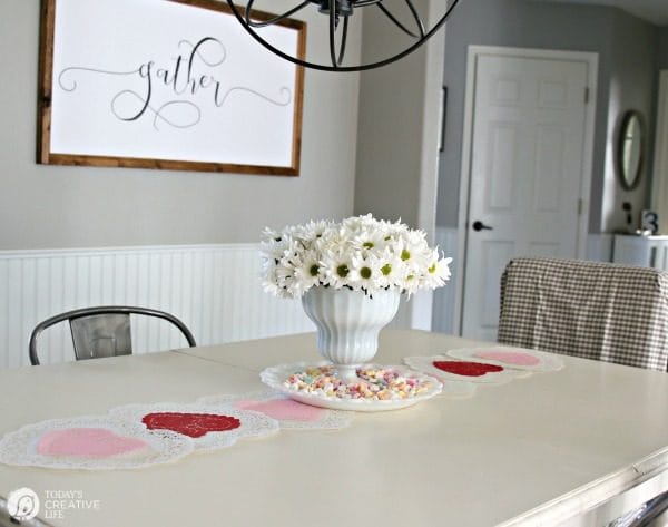 10 Minute Valentines Table Decor | create a quick, simple and easy Valentine's Day decorations tablescape centerpiece with a heart shape doily table runner, conversation hearts and daisies. See more on Today's Creative Life.