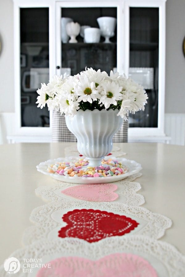 10 Minute Valentines Table Decor | create a quick, simple and easy Valentine's Day decorations tablescape centerpiece with a heart shape doily table runner, conversation hearts and daisies. See more on Today's Creative Life. 