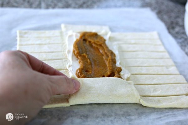 folding puff pastry dough around pumpkin cream cheese filling to create a puff pastry brraid
