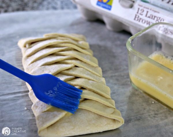brushing melted butter over an unbaked puff pastry braid