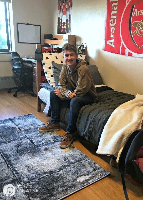 Dorm Room Ideas for Boys | Boy sitting on bedd in college dorm room. Decorated dorm room for guys.