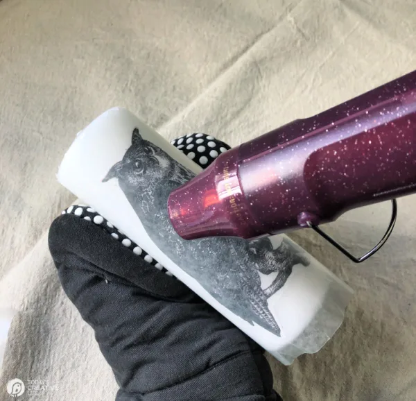 Hand in oven mitt using heat gun to blow hot air onto wax candle