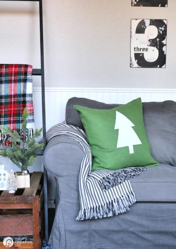 Green Pillow with white tree sitting on grey sofa.