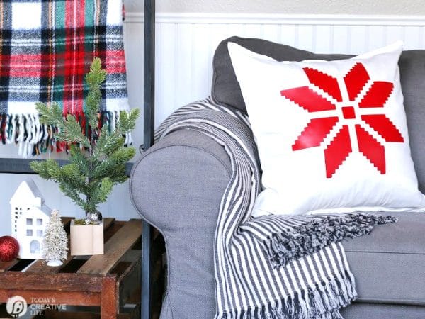 White pillow with Red Snowflake sitting on a grey sofa. 