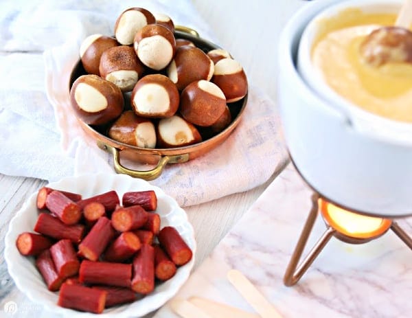 Cheese fondue pot with plates of pretzel balls and pepperoni