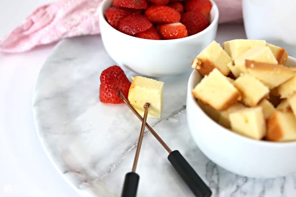 White bowls filled with strawberries and pound cake and fondue forks