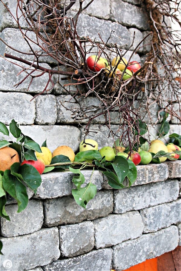 Outdoor fireplace with a twig wreath and apples on the mantel.