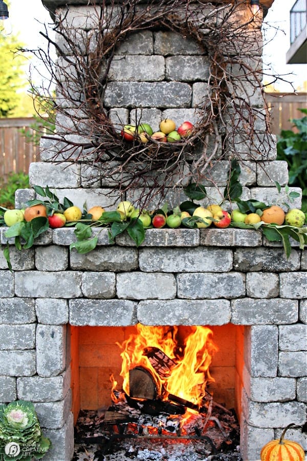 Outdoor stone fireplace with apples on the mantle and a roaring fire. 