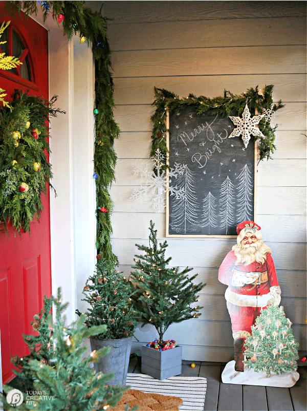 Christmas Porch Decorating Ideas with garland and a vintage Santa cutout.