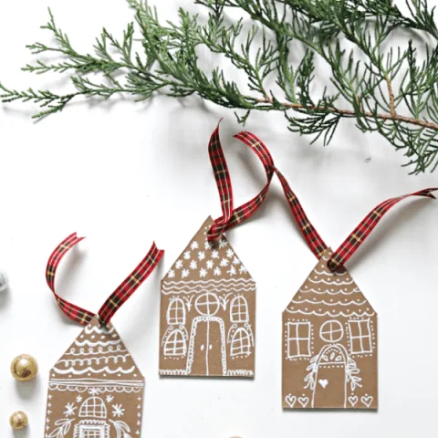 3 Gingerbread house DIY Christmas Ornaments made from chipboard or cardboard with white chalk marker drawings.