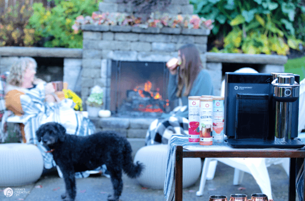 Outdoor setting with outdoor fireplace. 2 people chatting by the fire.