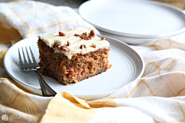 Piece of carrot cake with cream cheese frosting on a white plate.