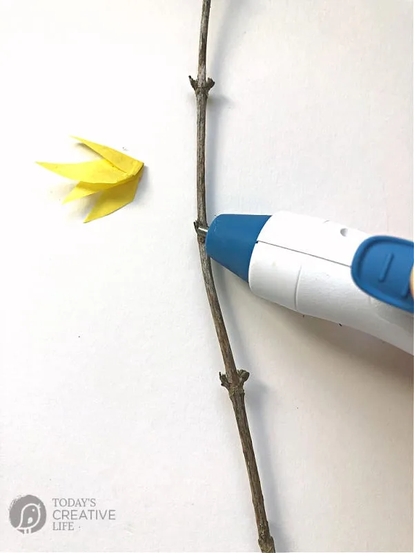 Using a hot glue gun to add glue to branch to apply tissue paper flower to.