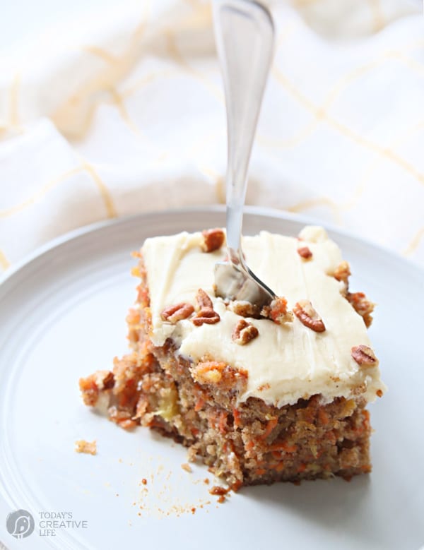 Carrot cake recipe with pineapple slice on white plate and a fork stuck straight up.