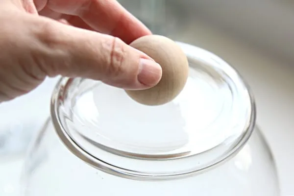 Hand placing wood ball knob on the bottom of a glass vase for making a cloche