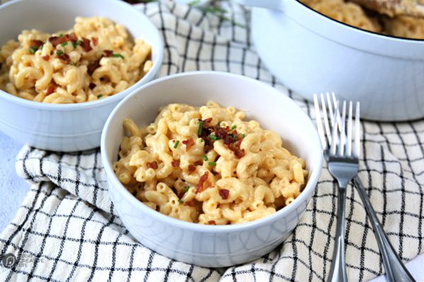 Recipe for Creamy Mac and Cheese served in white bowls. Bacon and chives for garnish