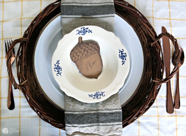 Ideas for Thanksgiving Table Settings | printed Paper acorn for place card with white bowl, plates on wicker charger. 