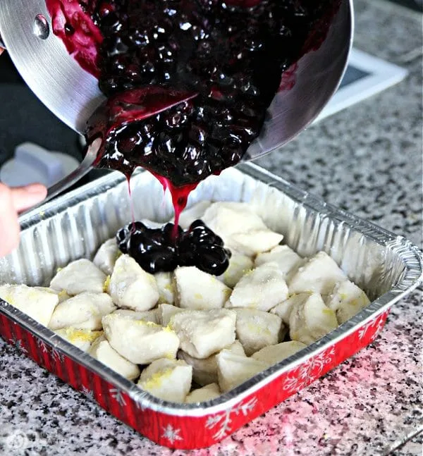 Blueberry pie filling being poured over quartered biscuits.