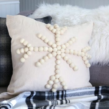 Cream colored decorative pillow with wool balls in the shape of a snowflake