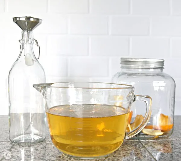 a clear glass bottle, a large glass measuring bowl and a jar with orange peels and vanilla beans for making infused vodka recipe