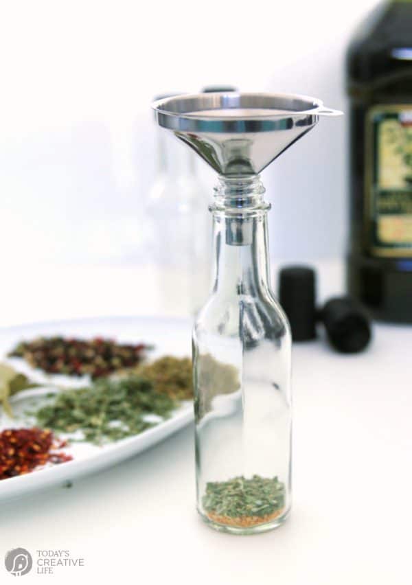 funnel over a glass bottle filled with herbs for how to infuse olive oil.
