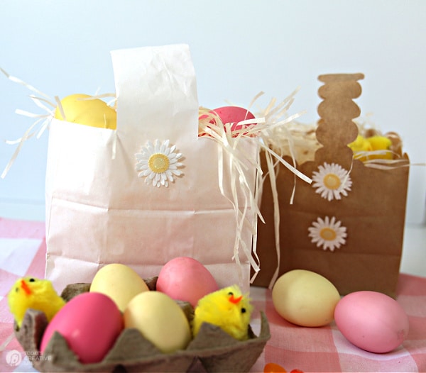 One white, one brown paper Easter baskets made using paper lunch sacks. Decorated with pink and yellow Easter eggs.