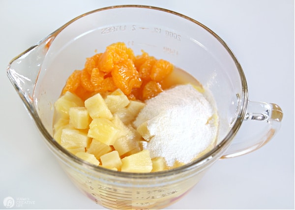 Glass bowl with pineapple, instant vanilla pudding and mandarin oranges for making vanilla pudding fruit cocktail salad.