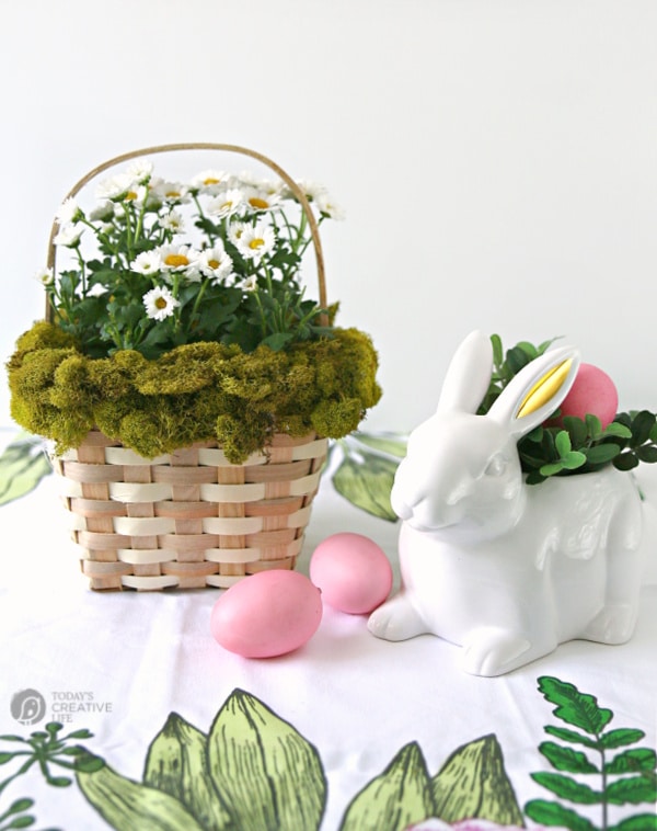 Basket decorated with Moss with a plant inside. White ceramic rabbit with pink eggs for easter decor.