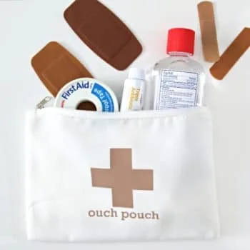 White cosmetic bag with iron-on vinyl saying Ouch Pouch, filled with first aid items