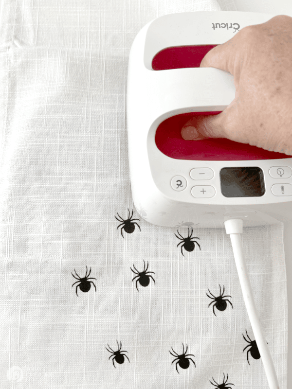 Cricut EasyPress ironing on vinyl spiders to table runner. DIY Halloween Decor