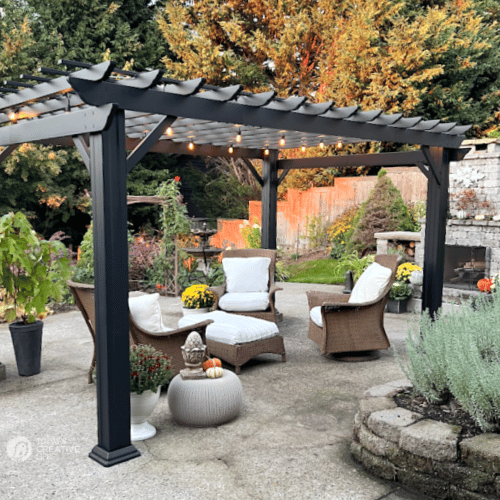 Black pergola with lights and light colored patio furniture.