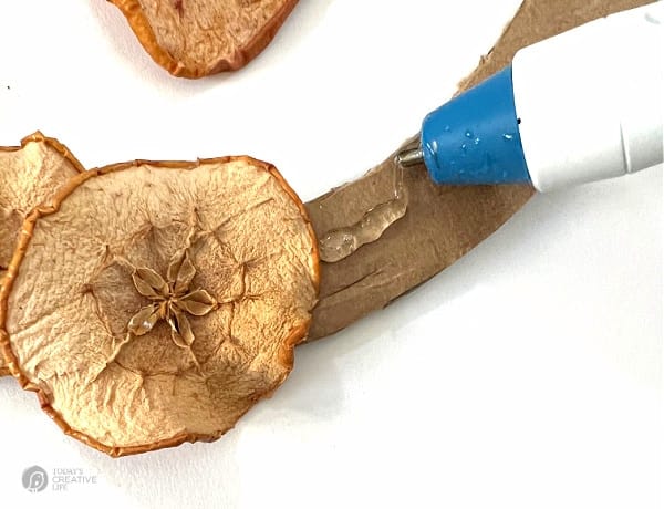 Gluing an apple slice to wreath with glue gun.