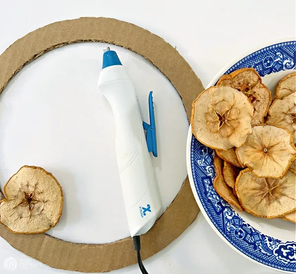 Cardboard wreath form with glue gun and apple slices for making a dried apple wreath.