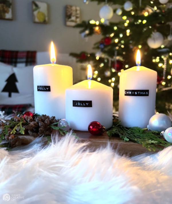 Three white candles with labels saying Holly Jolly Christmas.