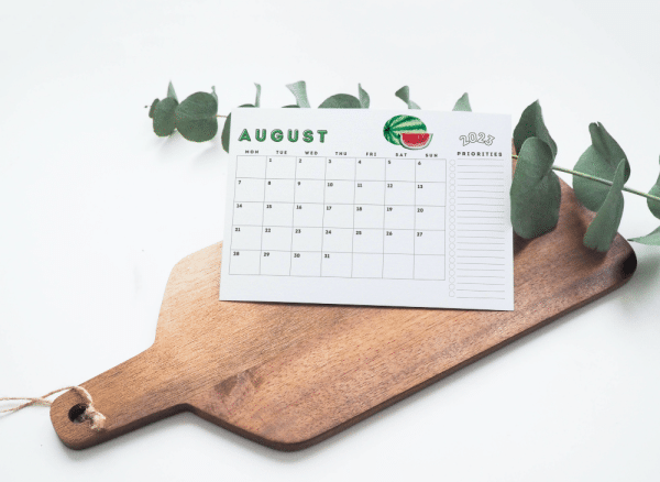 Brown cutting board with a printable calendar sheet propped up for a photo.