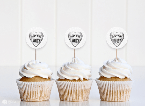 3 vanilla cupcakes with white frosting and LOVE ME cupcake toppers