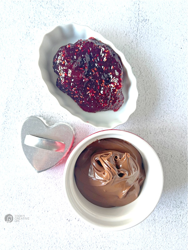 A heart shaped cookie cutter and Two bowls. Filled with raspberry jam, nutella