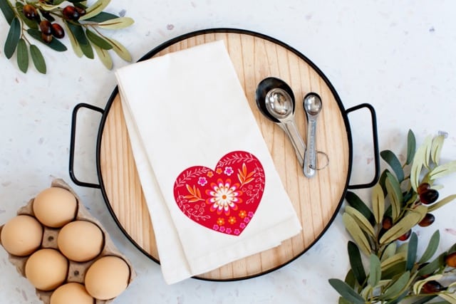 White dish towel with a red heart on a wood tray