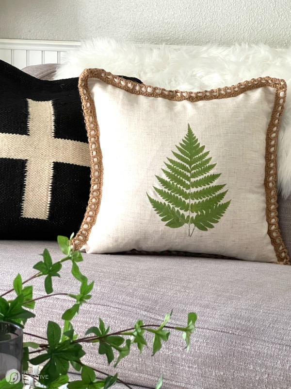 Two pillows on sofa. One pillow with a green fern. The other pillow is black with white cross.