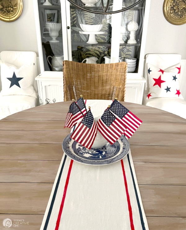 Table with a fabric painted patriotic table runner with a red and blue stripe along the edges. 