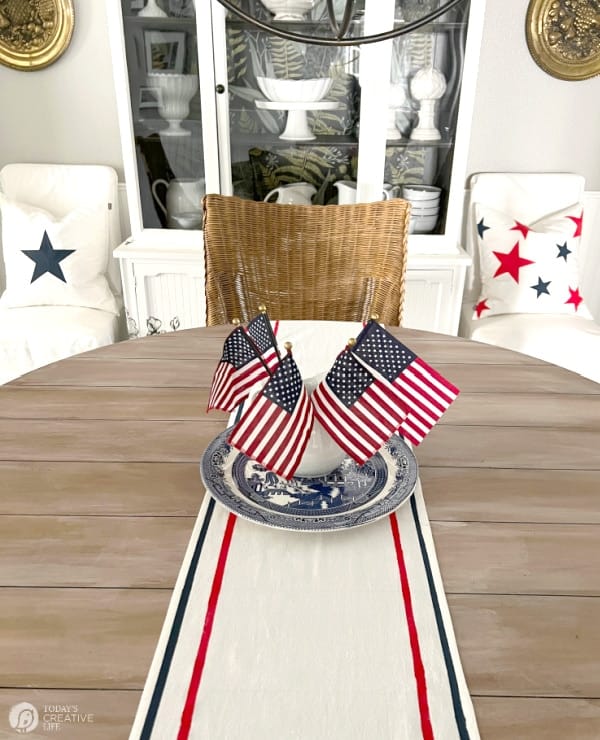 Table with a fabric painted patriotic table runner with a red and blue stripe along the edges. 