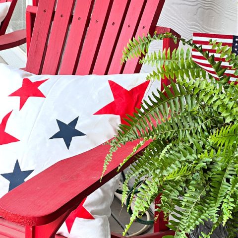 White pillow with red and blue stars painted on, sitting on a red chair.